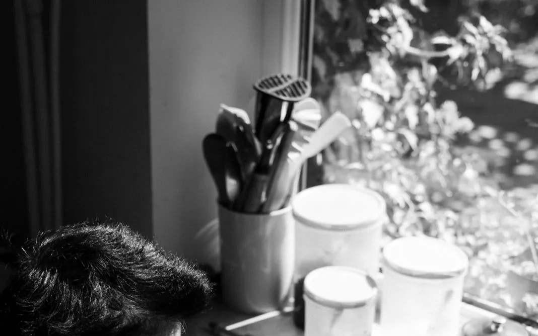 Une femme âgée prépare à manger dans sa cuisine, près d’une fenêtre ensoleillée